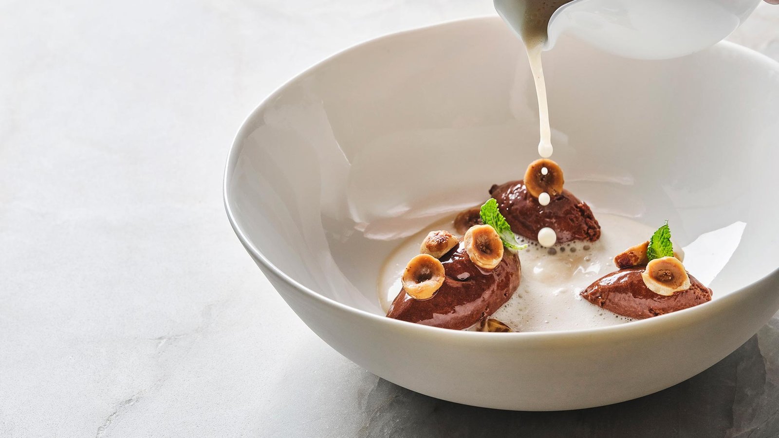 Postre de mousse de chocolate con avellanas y espuma, servido con jarra.