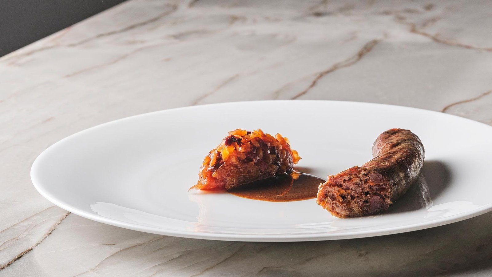 Butifarra con compota sobre plato blanco y encimera de mármol.