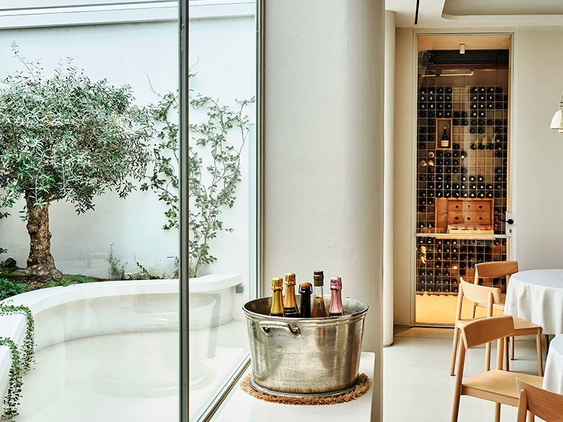 Cubitera con vinos junto a la bodega acristalada, con el olivo del patio al fondo.